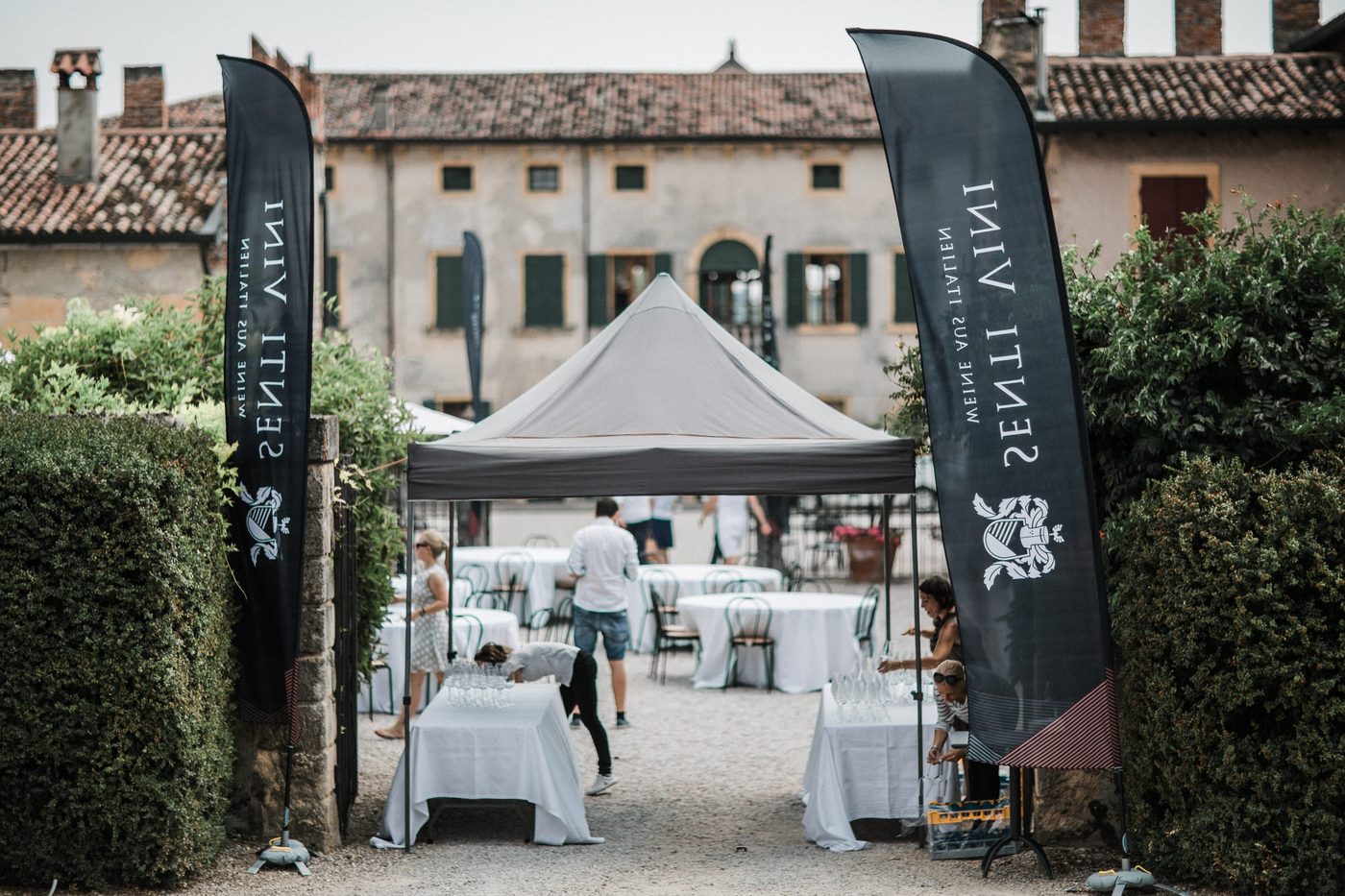 Eingangsbereich mit Senti Vini Flaggen und gedeckten Tischen beim Sommerfest 2017 in Italien