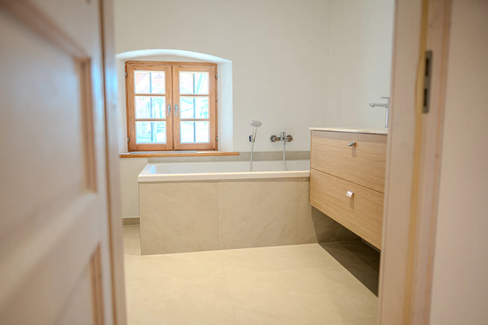 Badezimmer mit Badewanne, Waschtisch und Holzfenster im renovierten Altbau